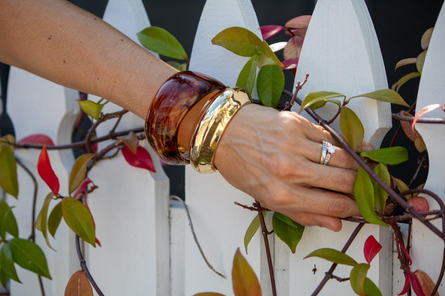 Hand with bracelets and a ring on a white picket fence background