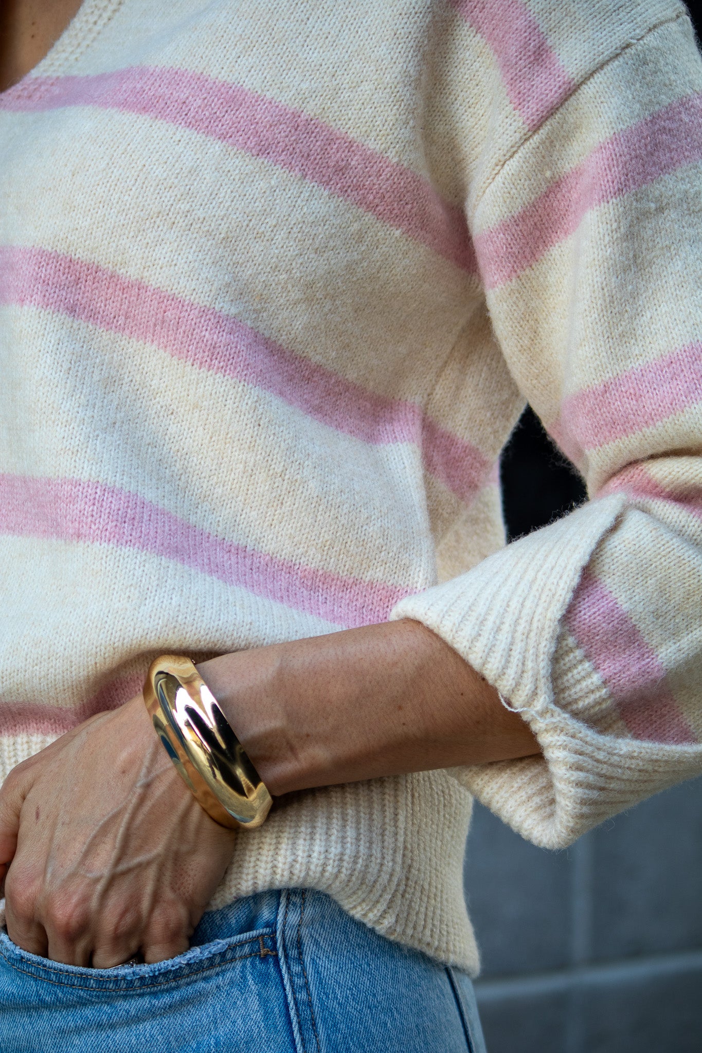 Close-up of a person wearing a striped sweater and gold bracelet.