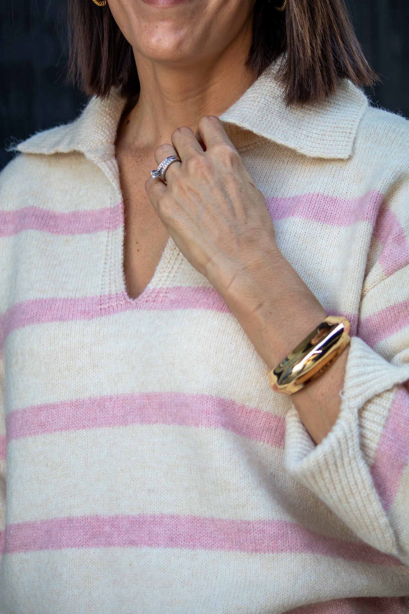 Person wearing a pink and white striped sweater with a gold watch and ring.