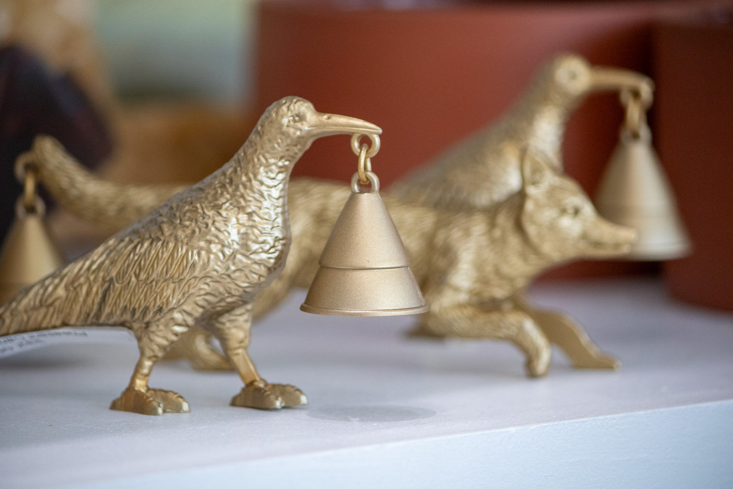 Gold bird-shaped candle snuffer on a white surface with a blurred background