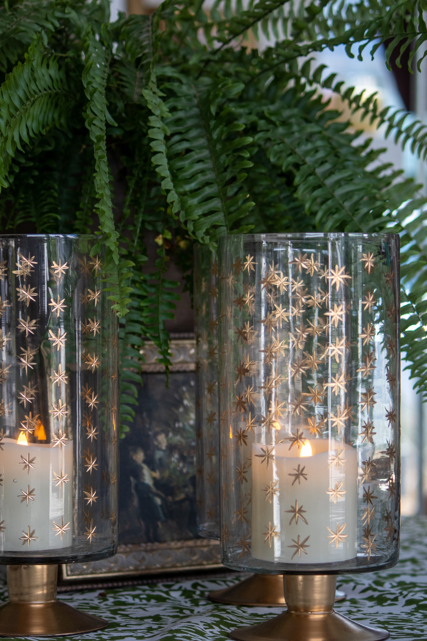 Decorative glass candle holders with star patterns on a table with ferns in the background.
