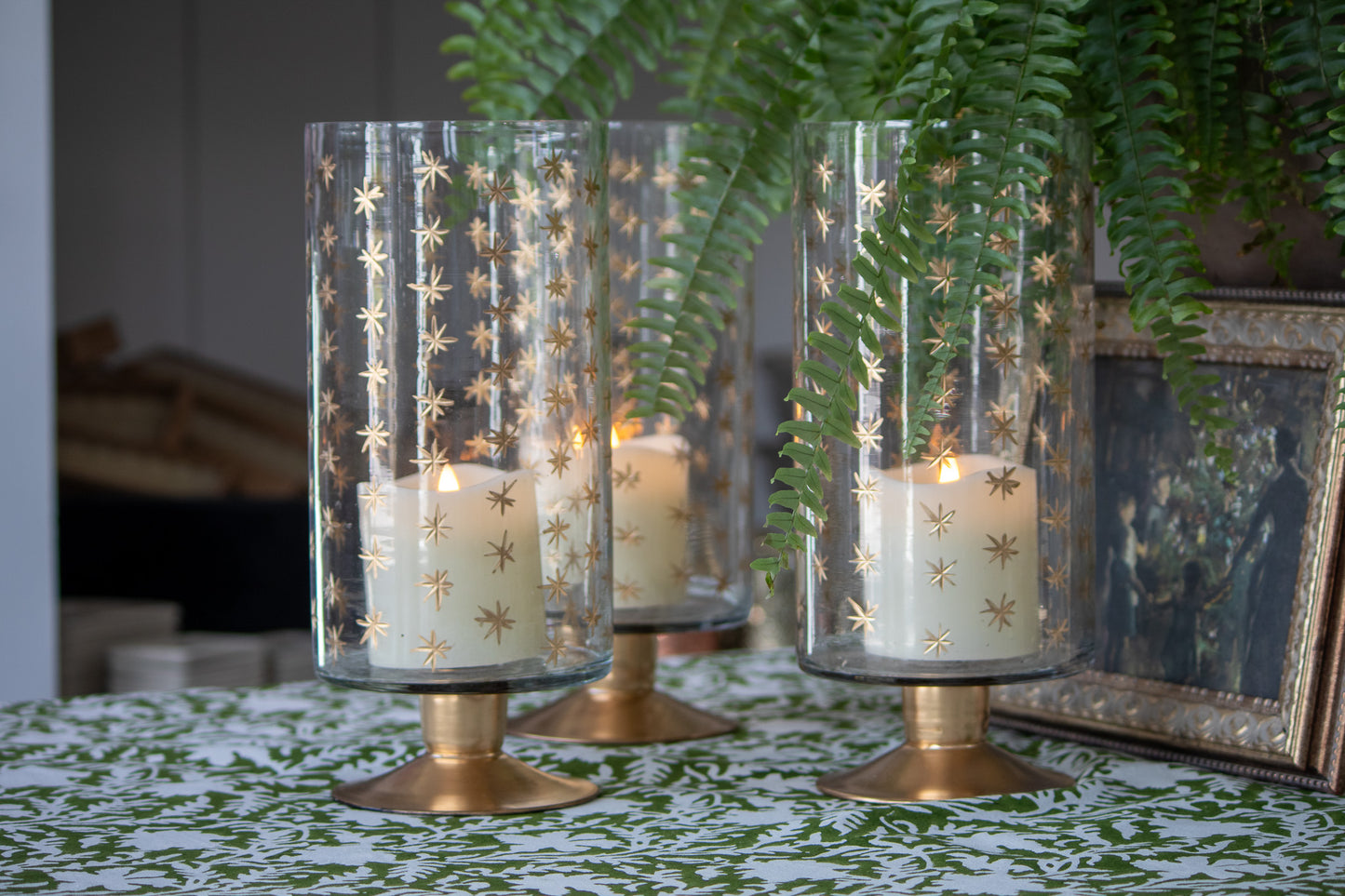 Decorative candle holders with gold star patterns on a table with a plant in the background.