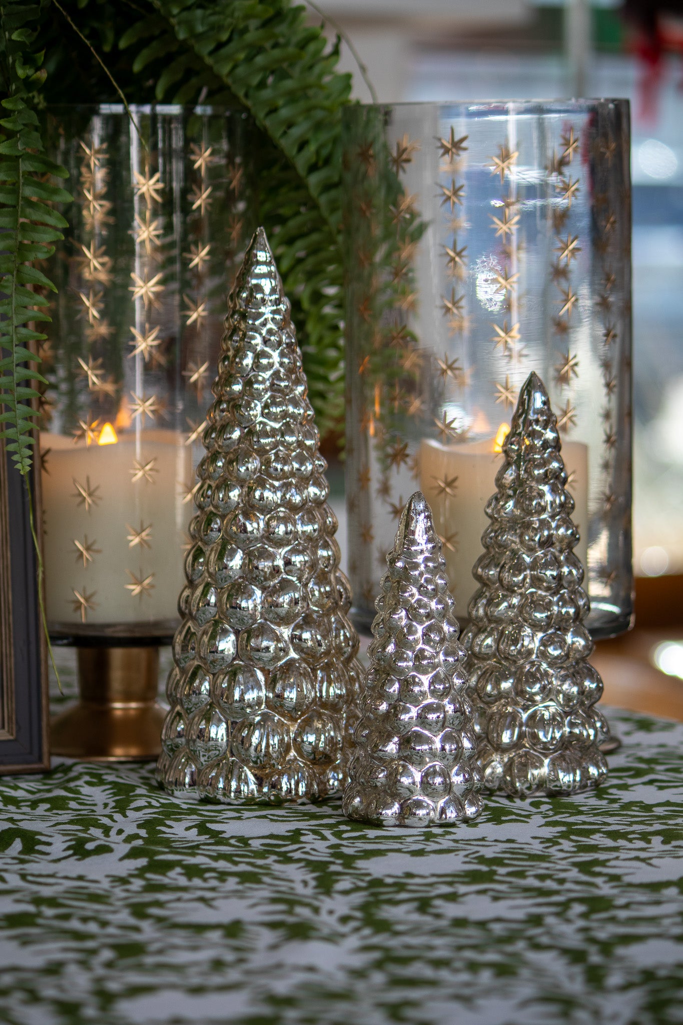 Decorative silver Christmas trees in front of glass candle holders with star patterns.