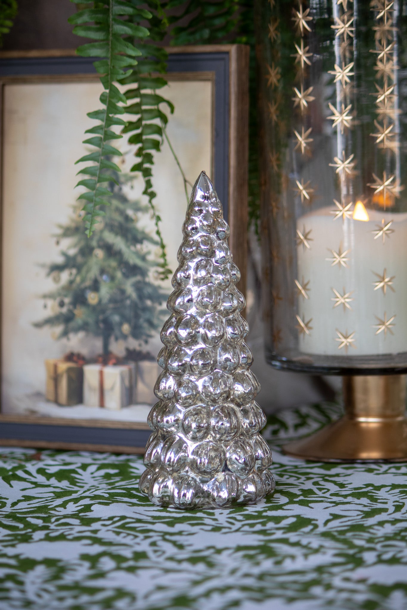 Decorative glass Christmas tree on a table with a candle and framed picture in the background