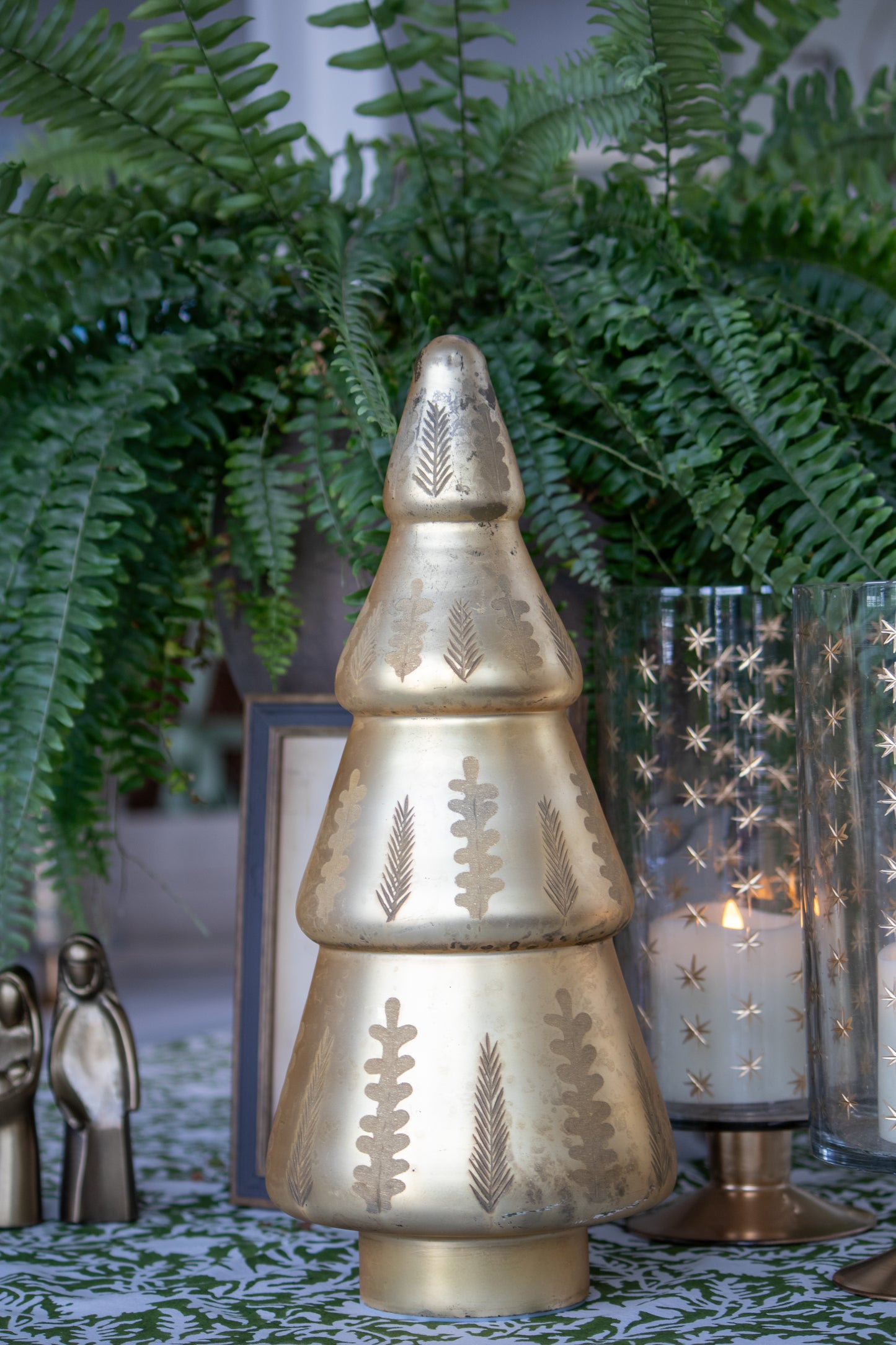 Decorative gold tree-shaped with candle holder and ferns and candles in the background