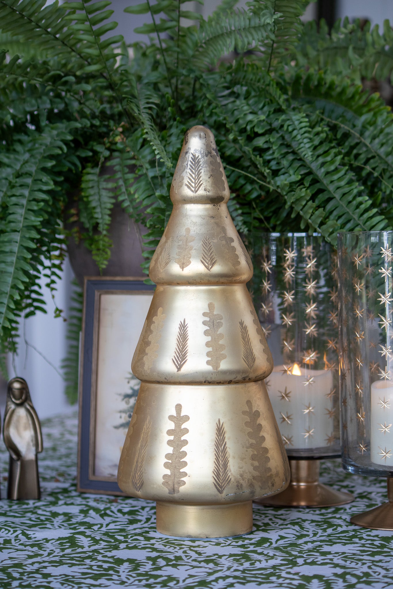 Decorative gold Christmas tree, candle holder, ferns and candles in the background