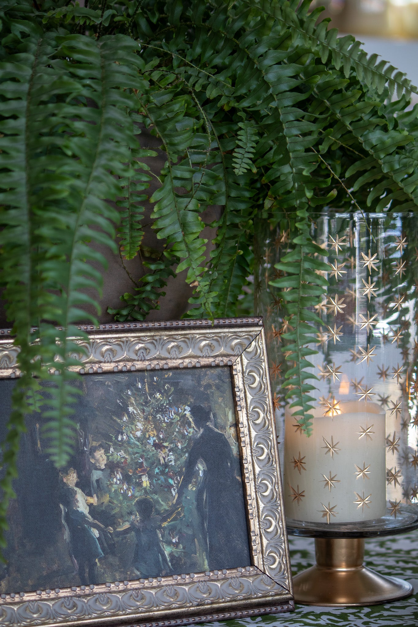 Decorative table setting with a framed painting, candle, and ferns.
