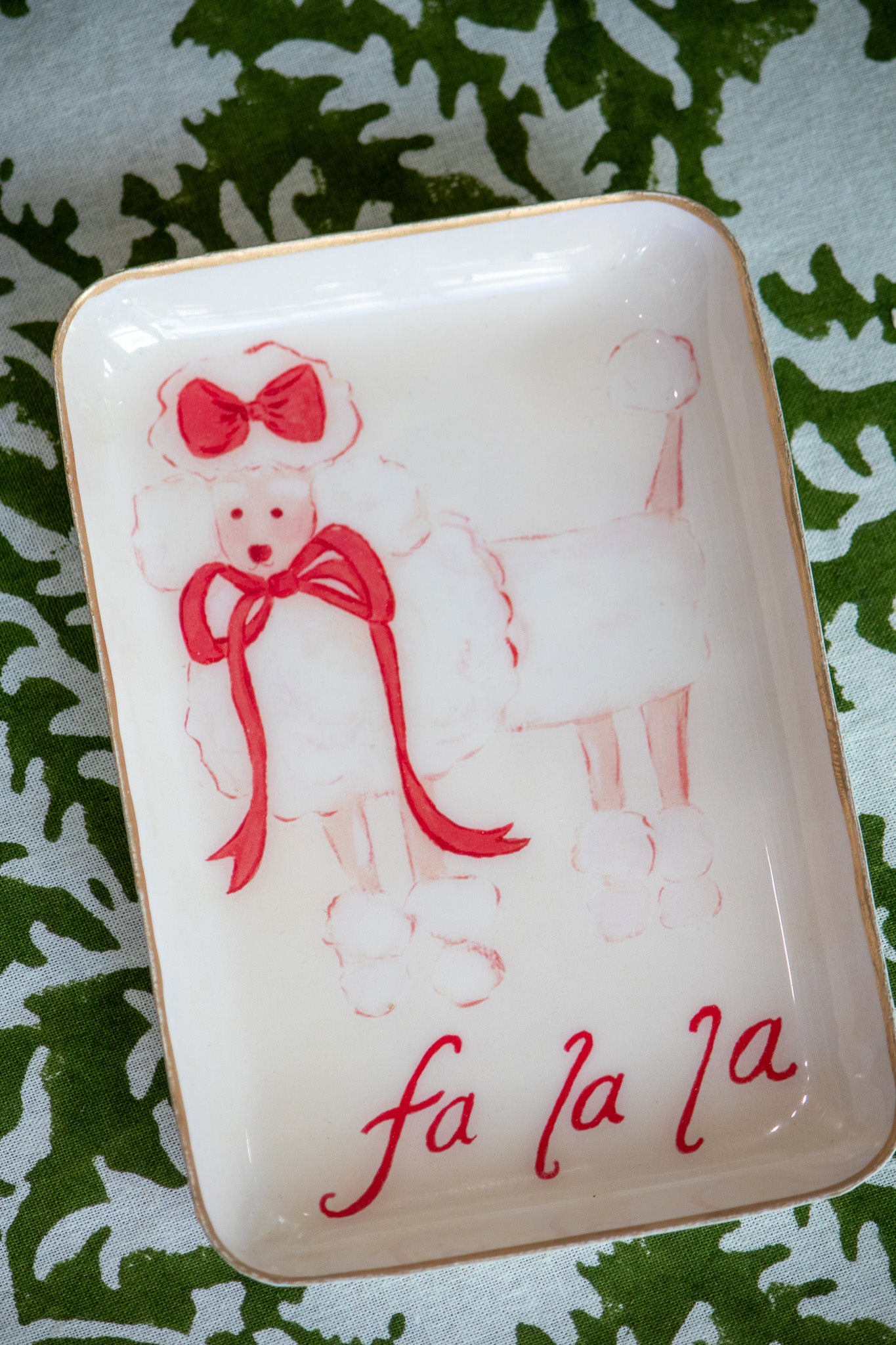 Decorative tray with a poodle illustration and 'fa la la' text sitting on a green and white tablecloth.