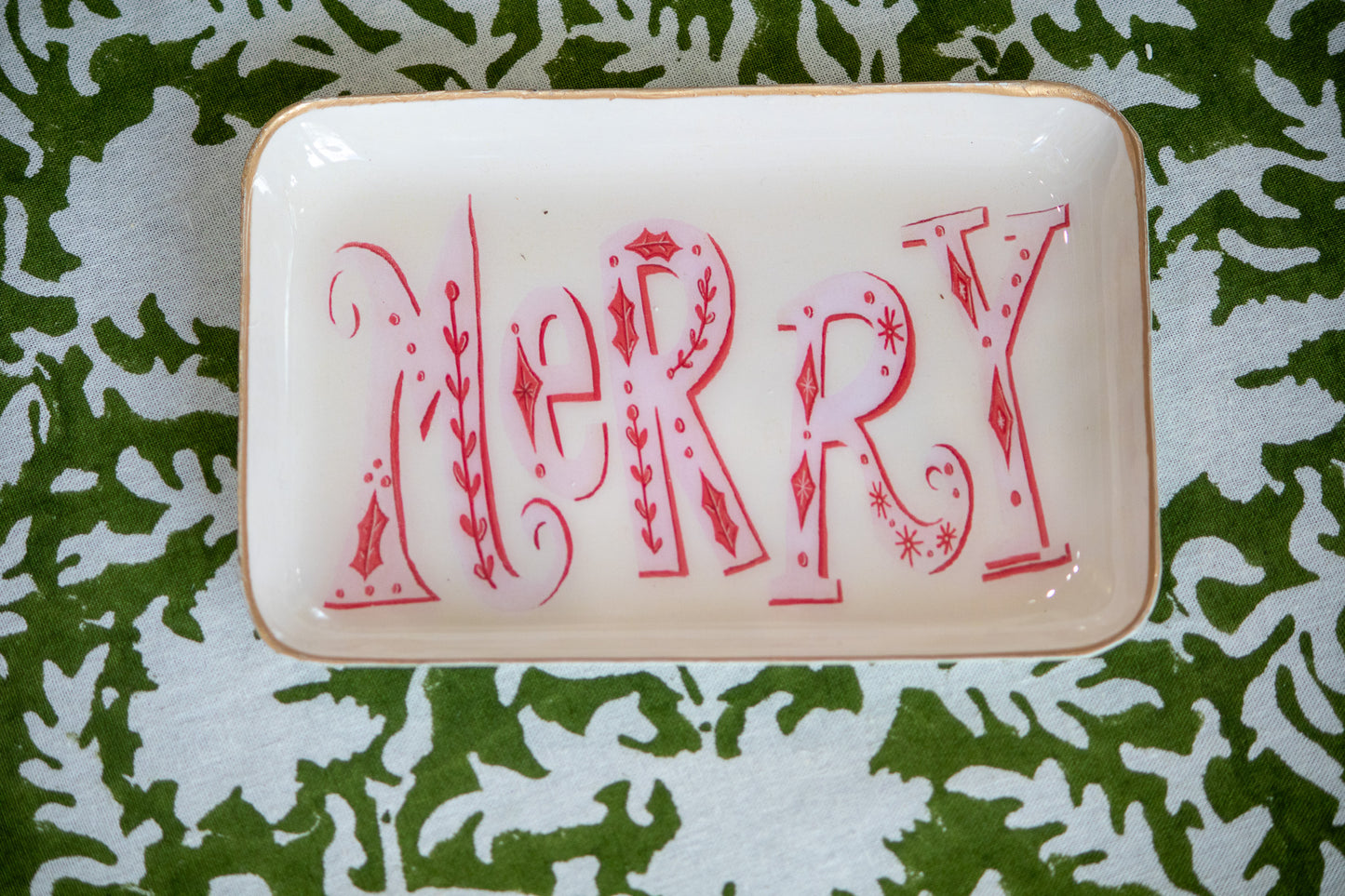 Decorative tray with 'MERRY' in red letters sitting on green and white patterned table cloth