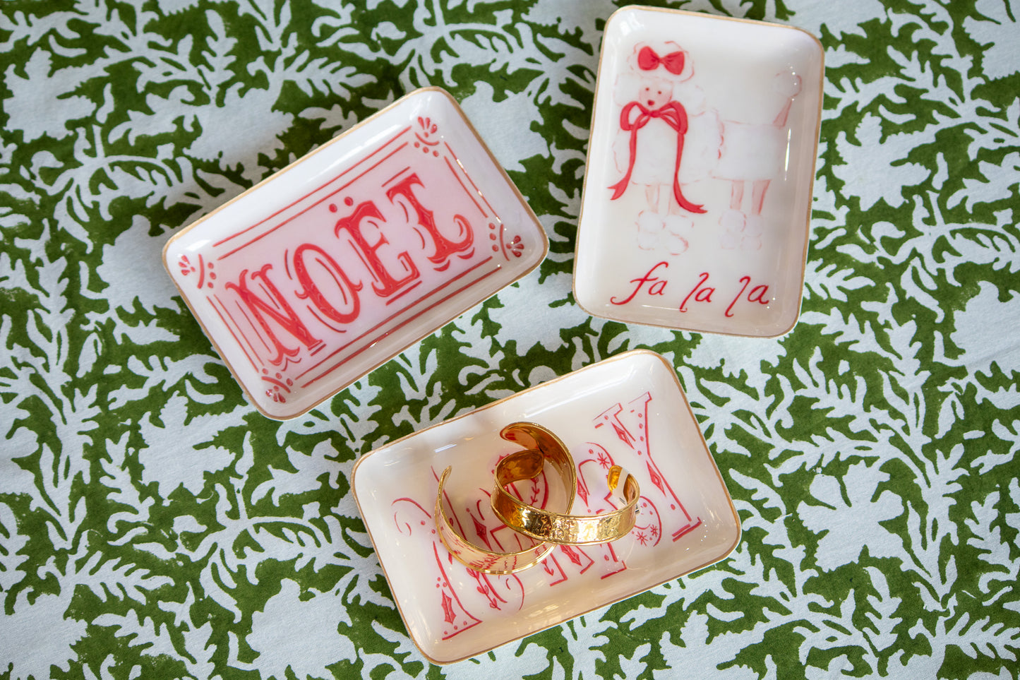 Three decorative metal trays with festive designs on a green and white patterned surface.