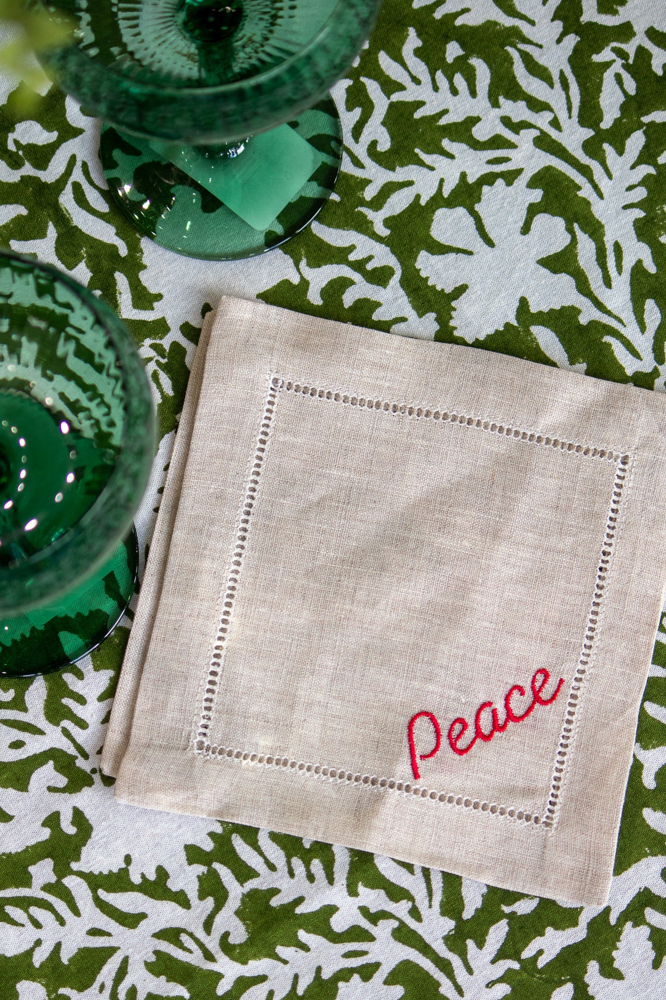 Linen Coaster with 'Peace' embroidery on a green and white patterned tablecloth