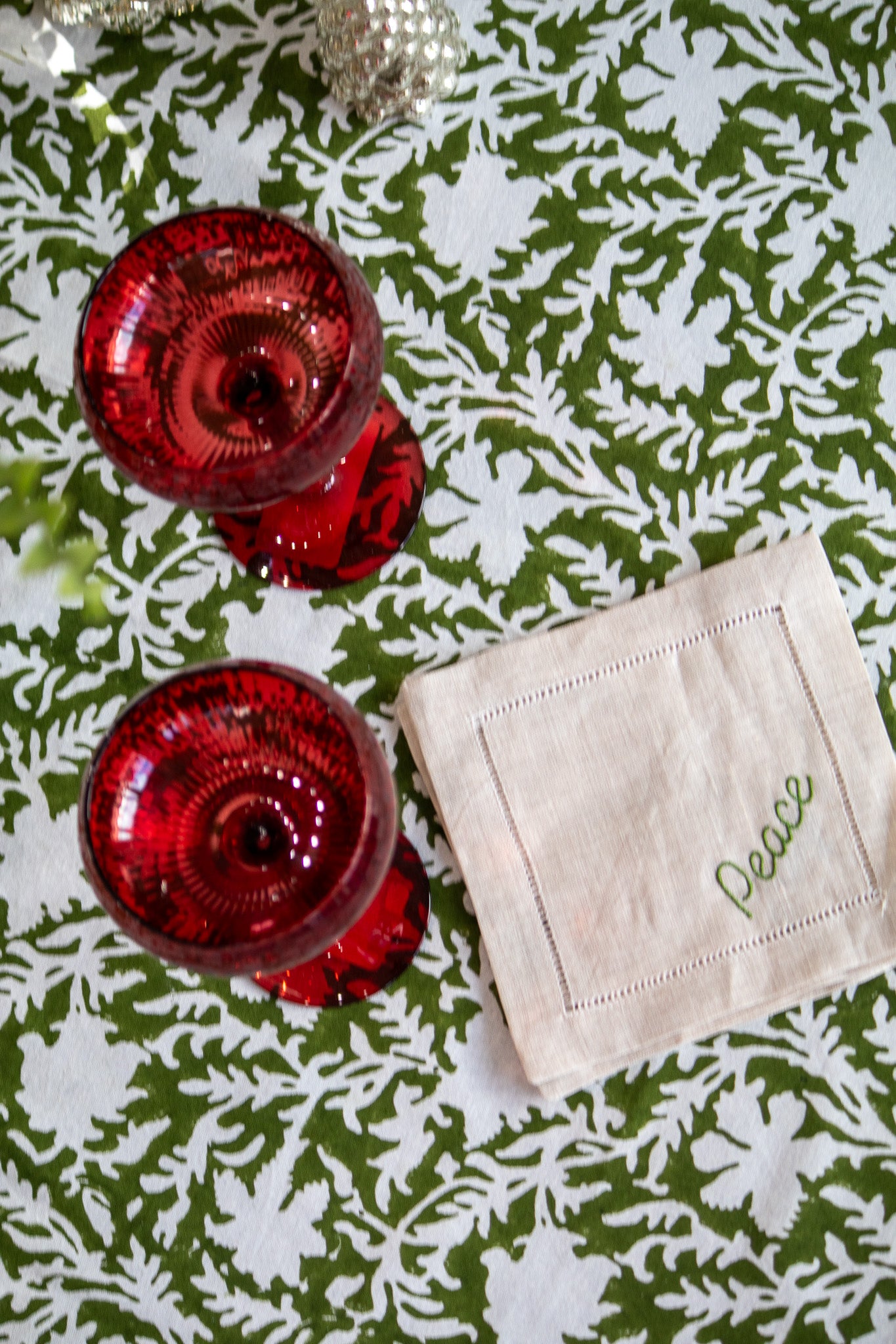 Red glassware and a beige coaster with 'Peace' on a green and white patterned tablecloth.