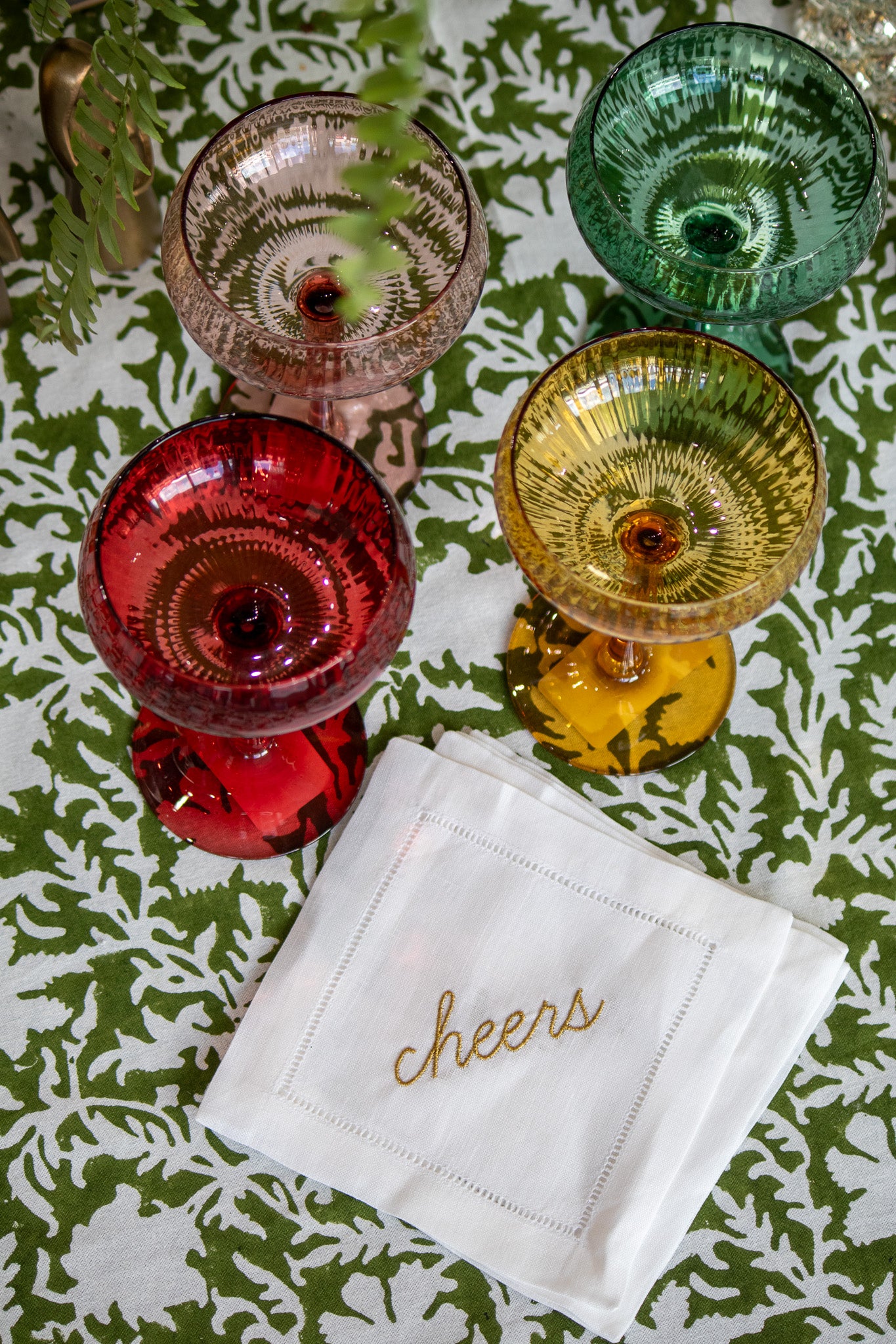 Colorful glassware with a 'cheers' napkin on a patterned tablecloth