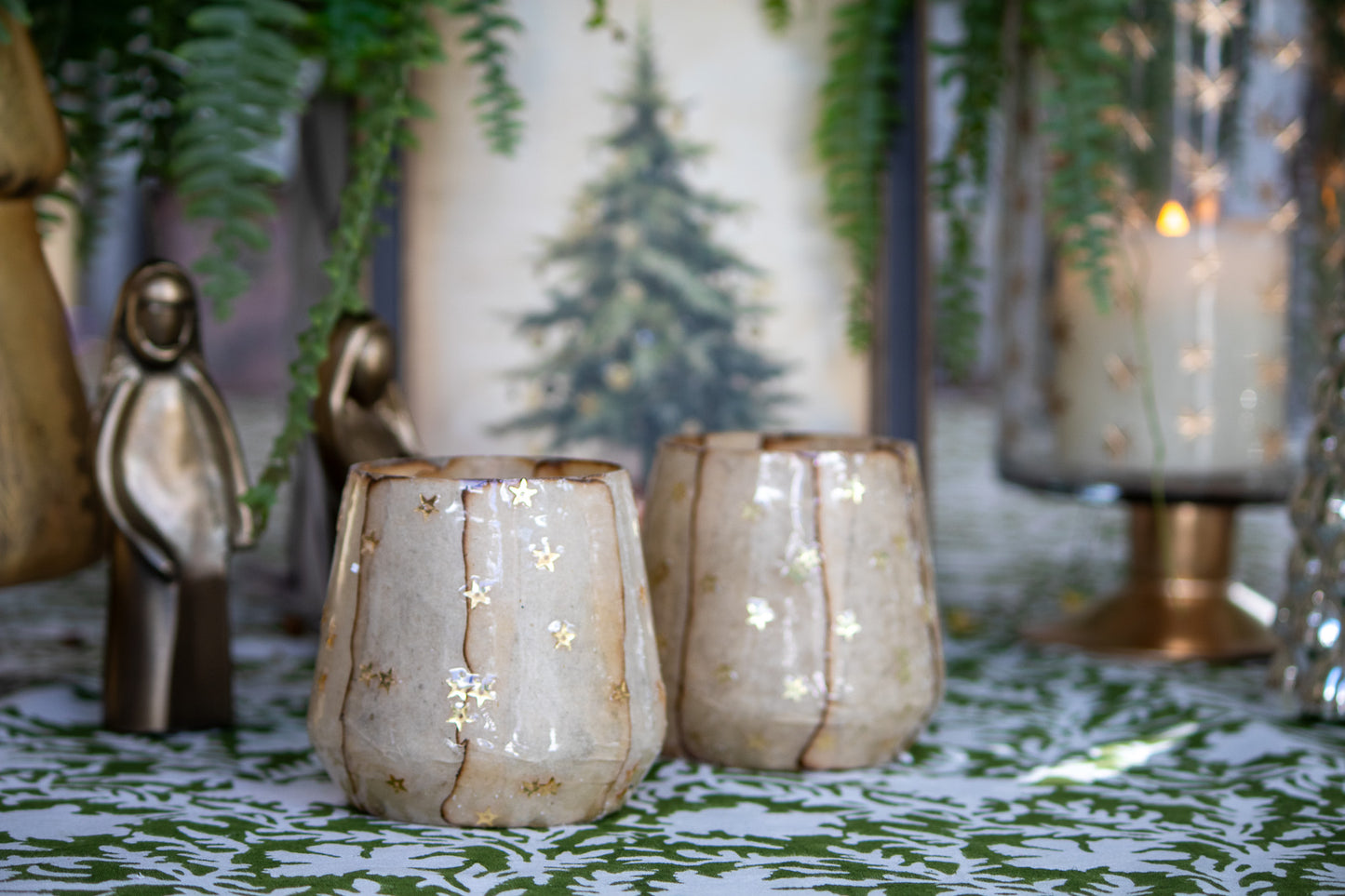 Decorative candles in ceramic holders on a patterned surface with greenery in the background