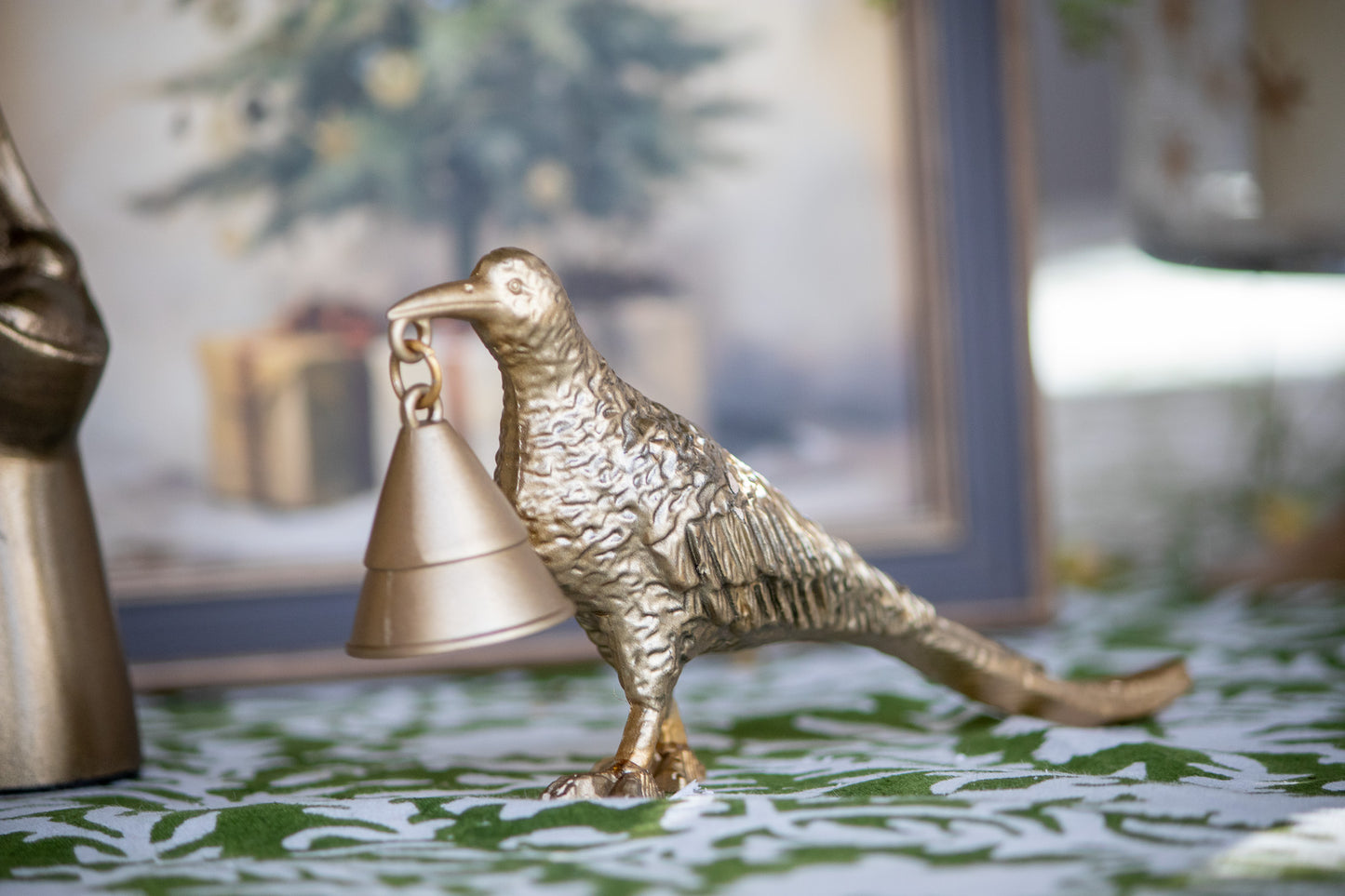 Bronze pheasant-shaped candle snuffer on a decorative surface with a blurred background