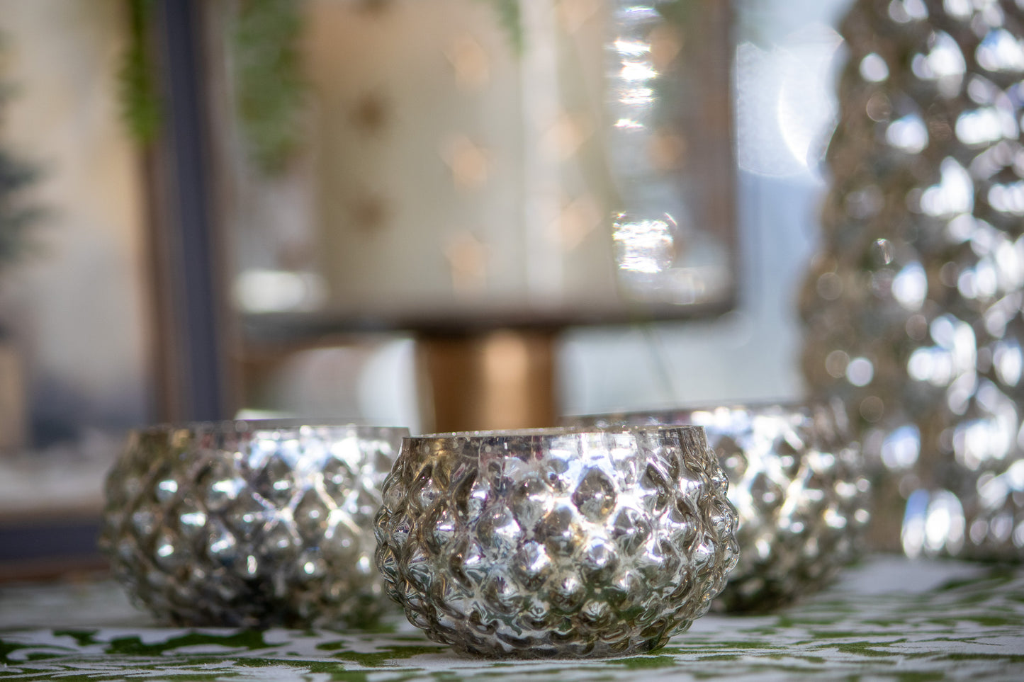 Silver textured candle holders on a decorative surface with blurred background