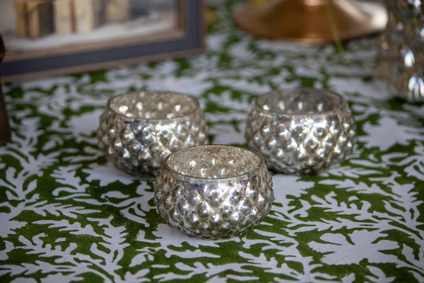 Three silver textured candle holders on a green and white patterned tablecloth.