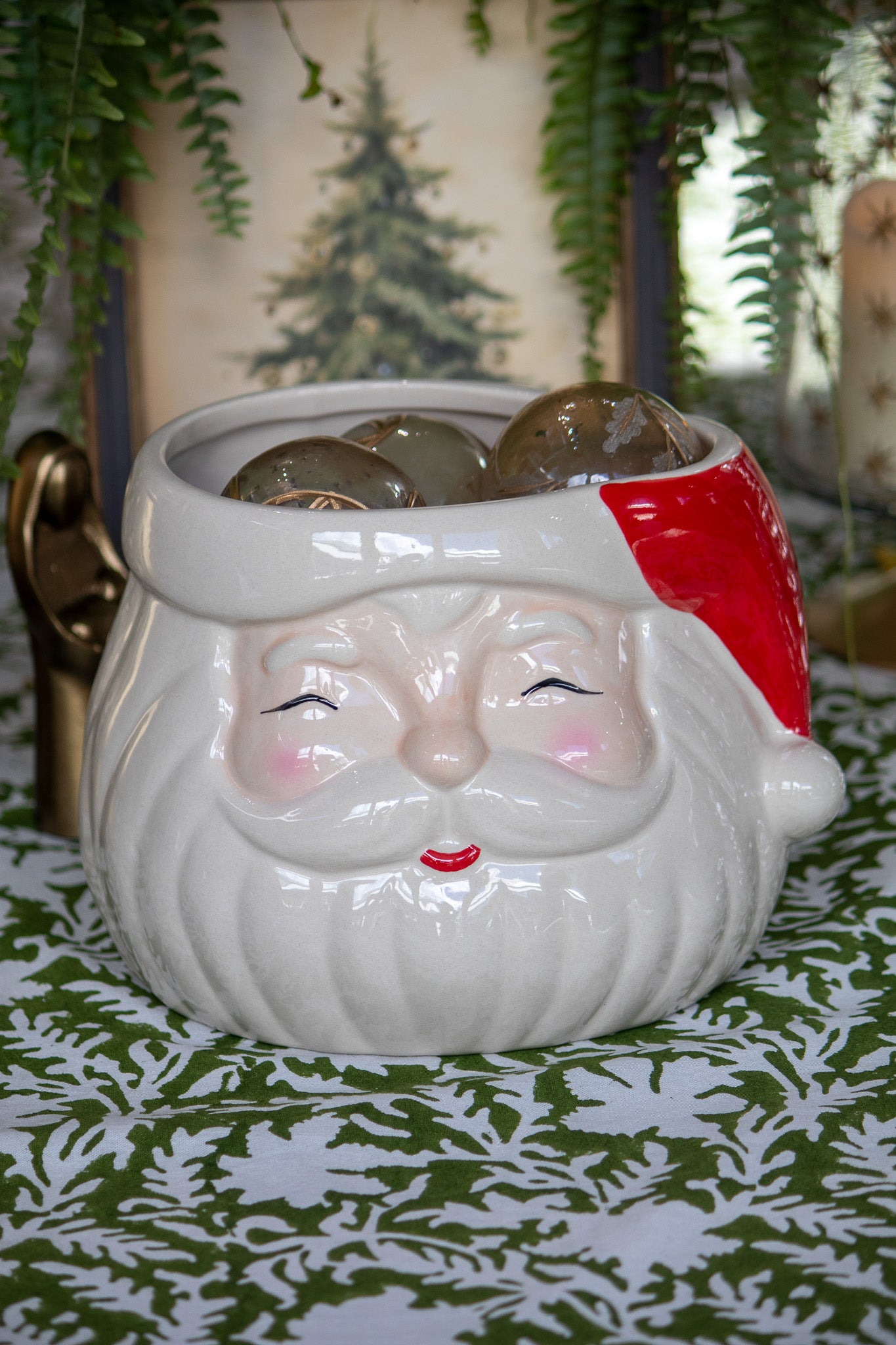 Ceramic pot shaped like a Santa face with a red hat on a green surface.