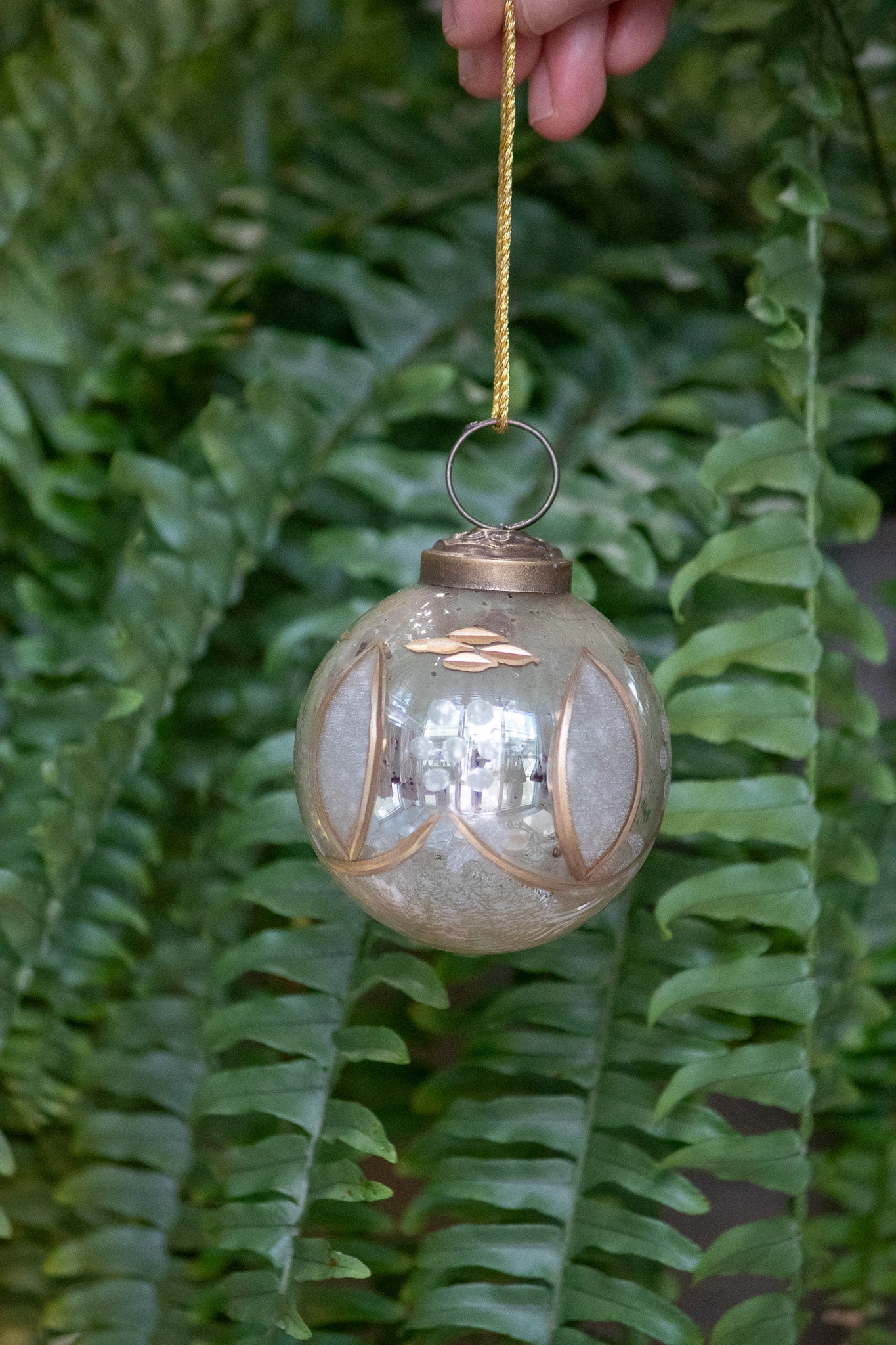Decorative glass ornament with gold accents hanging against a fern background