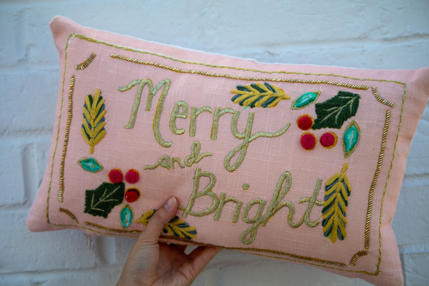Pink pillow with embroidered 'Merry and Bright' text and festive designs.