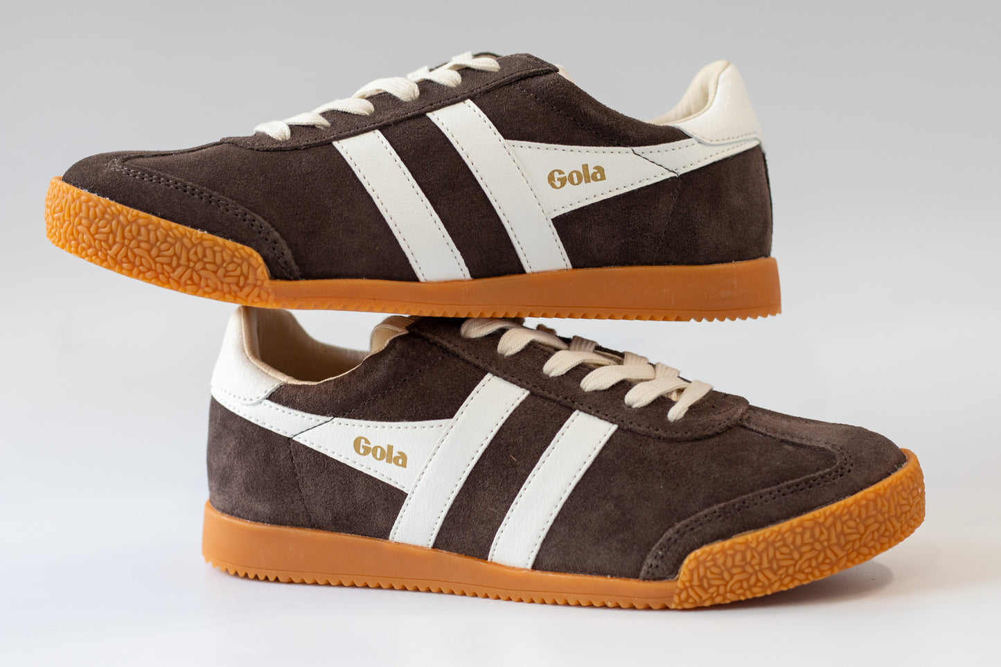 Pair of brown Gola sneakers with white stripes on a light gray background