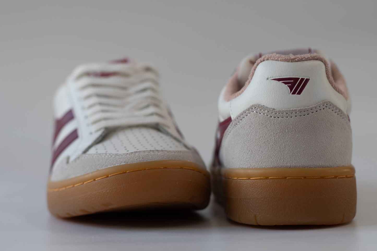 Pair of white sneakers with maroon accents on a light gray background