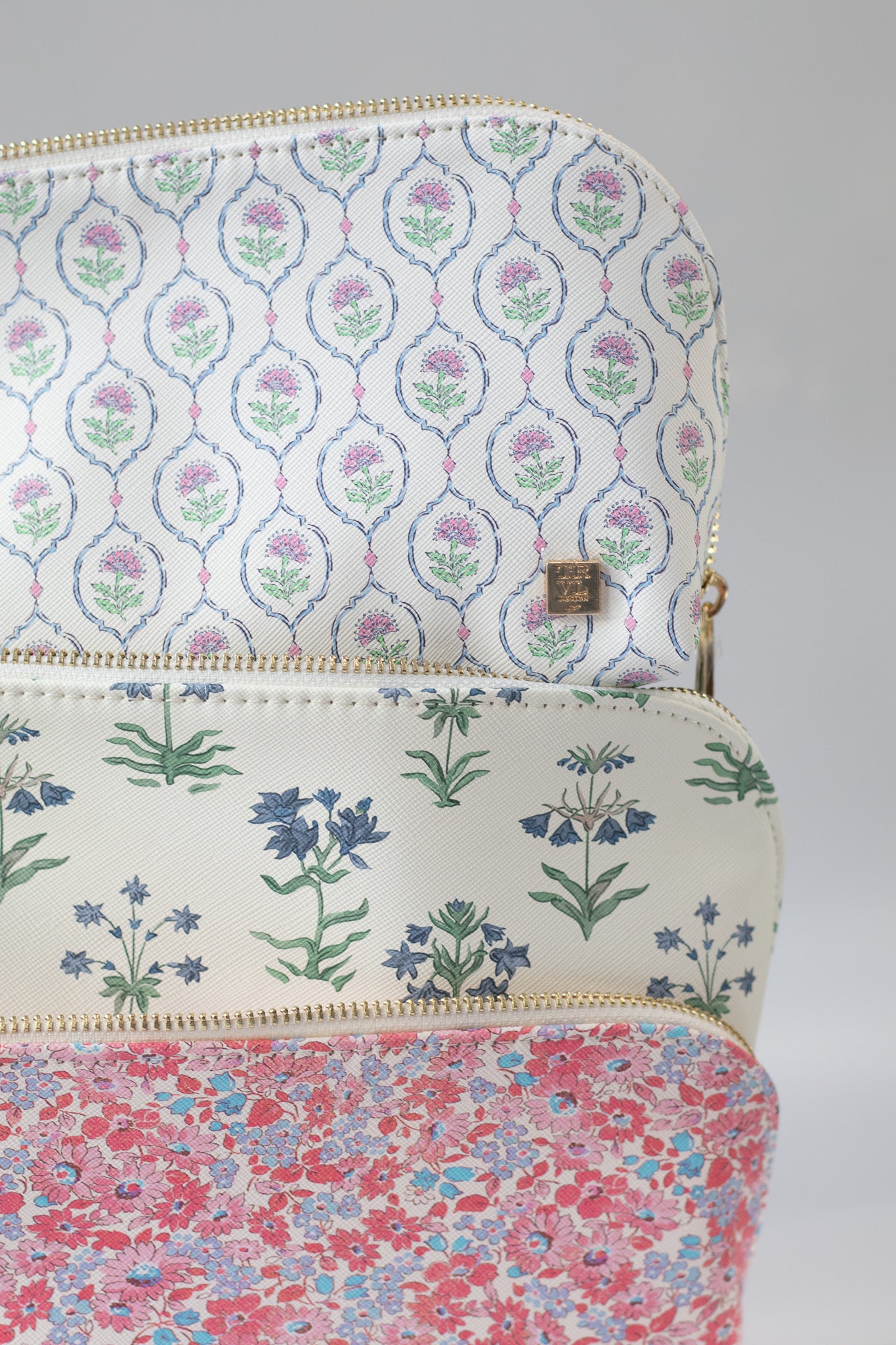 Three floral-patterned pouches stacked on a gray background