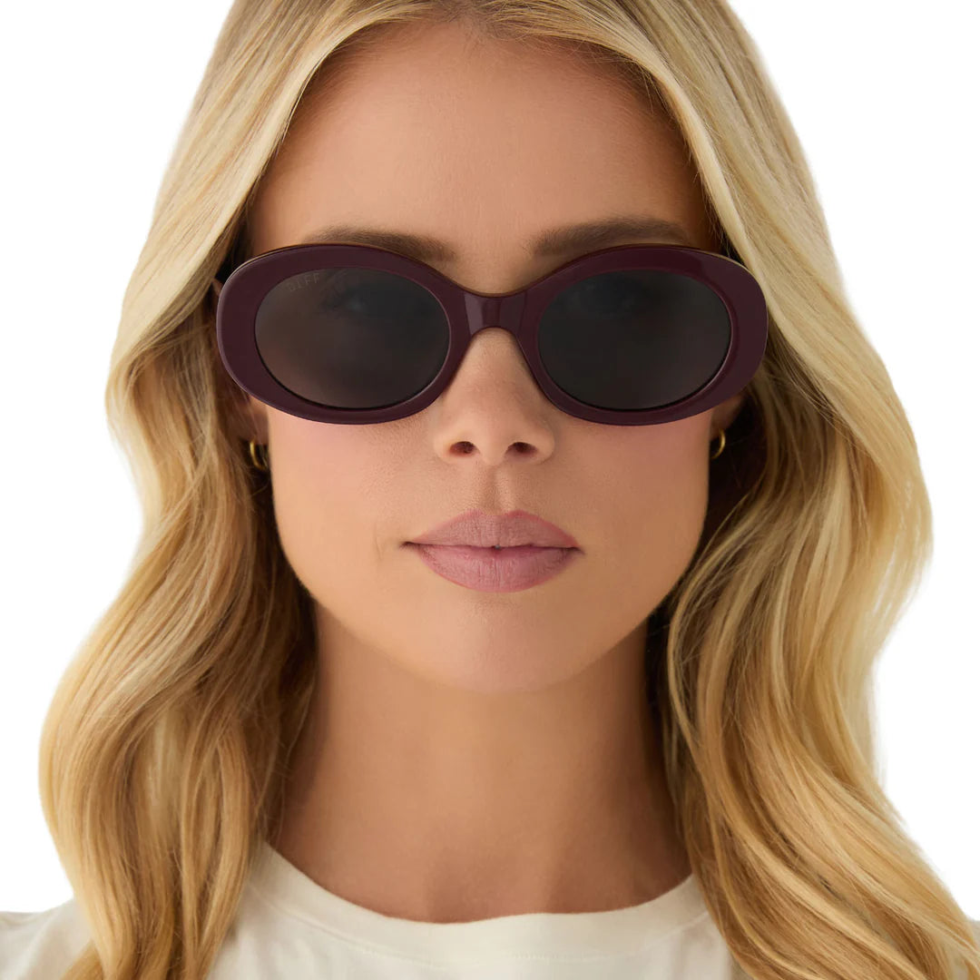 Woman wearing a pair of round sunglasses with a white background