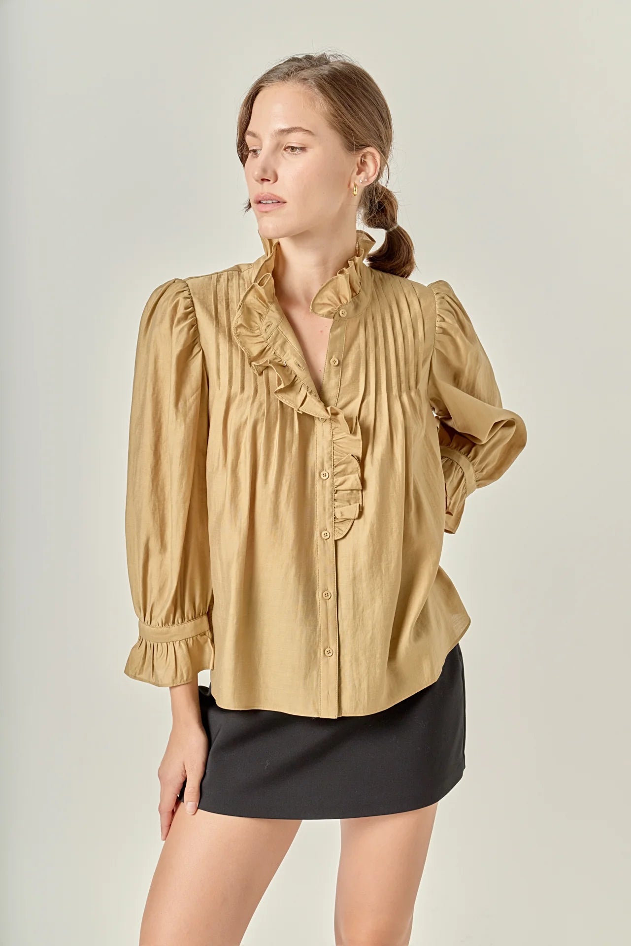 Woman wearing a beige blouse with ruffled details and a black skirt on a plain background