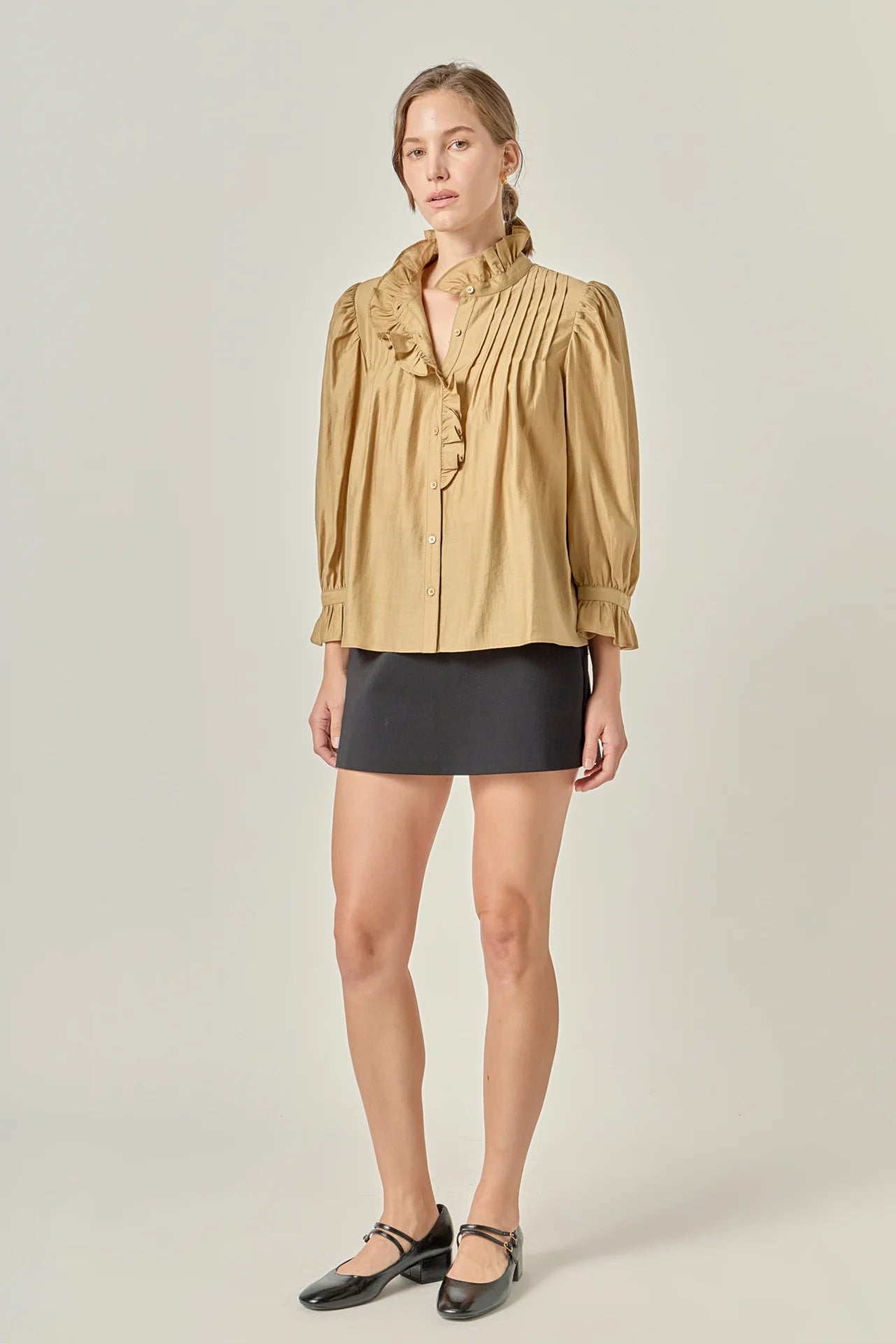 Woman wearing a beige blouse with ruffled details and a black skirt on a plain background