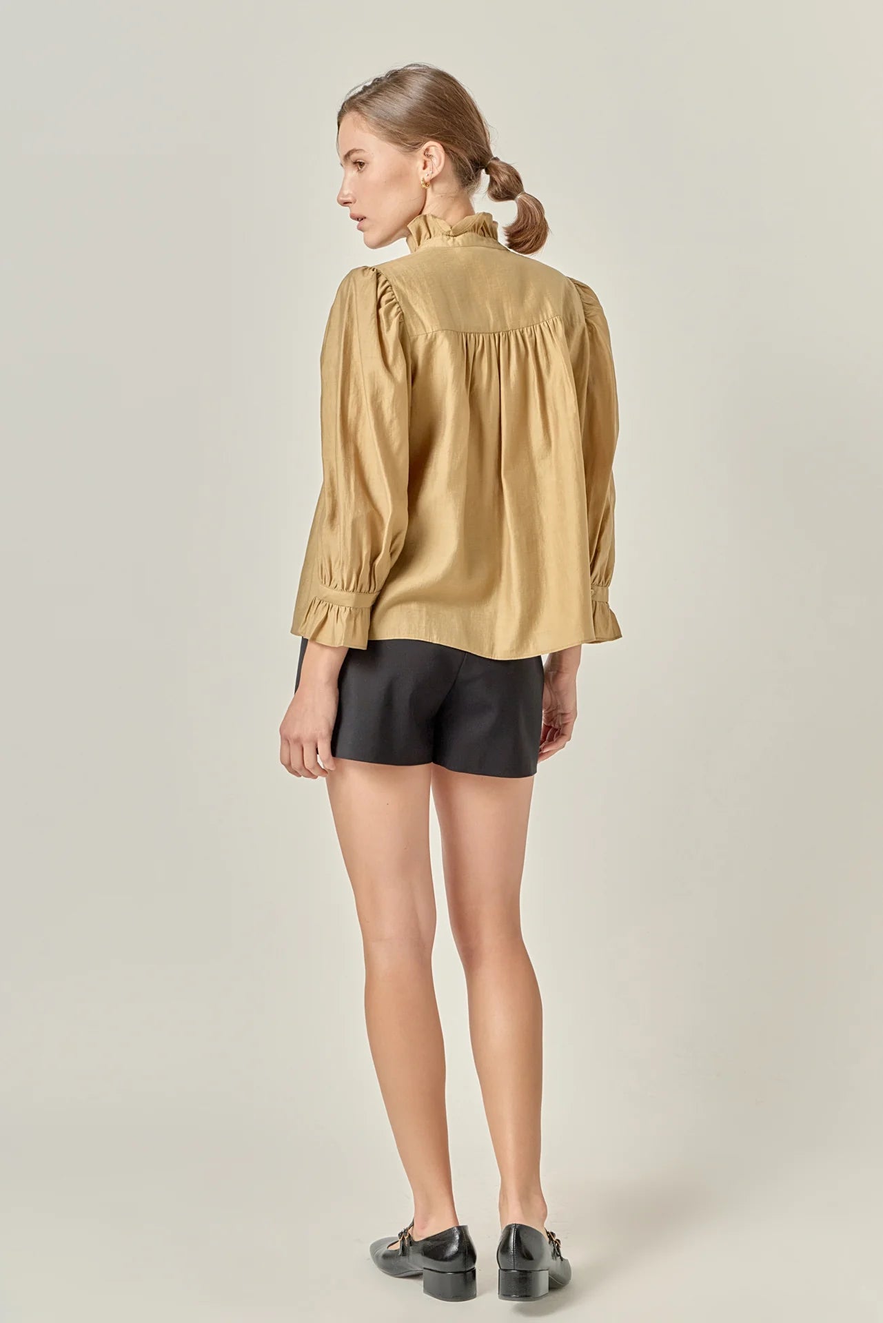Woman wearing a beige blouse and black shorts on a plain background