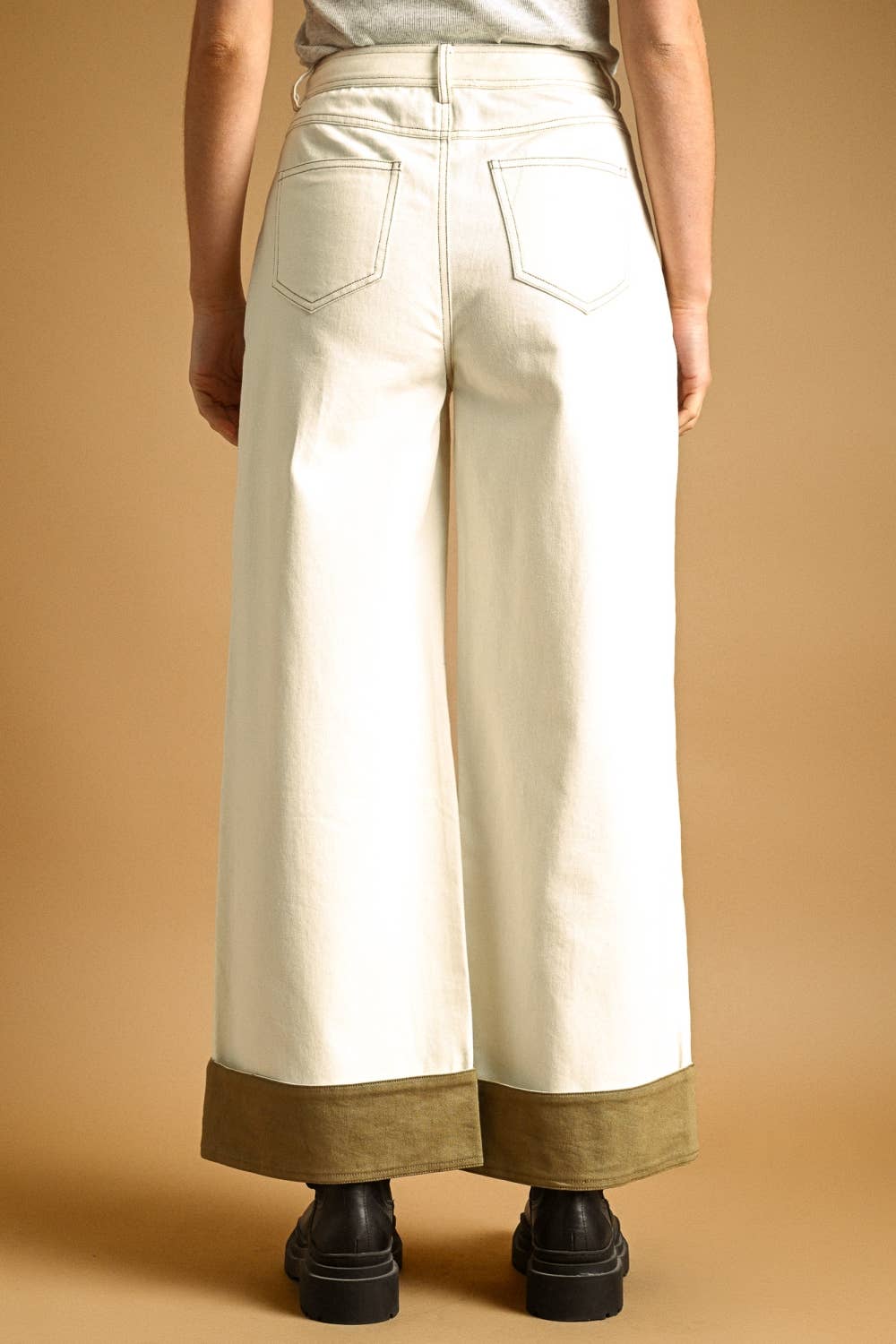 Person wearing white wide-leg pants with brown trim on a beige background