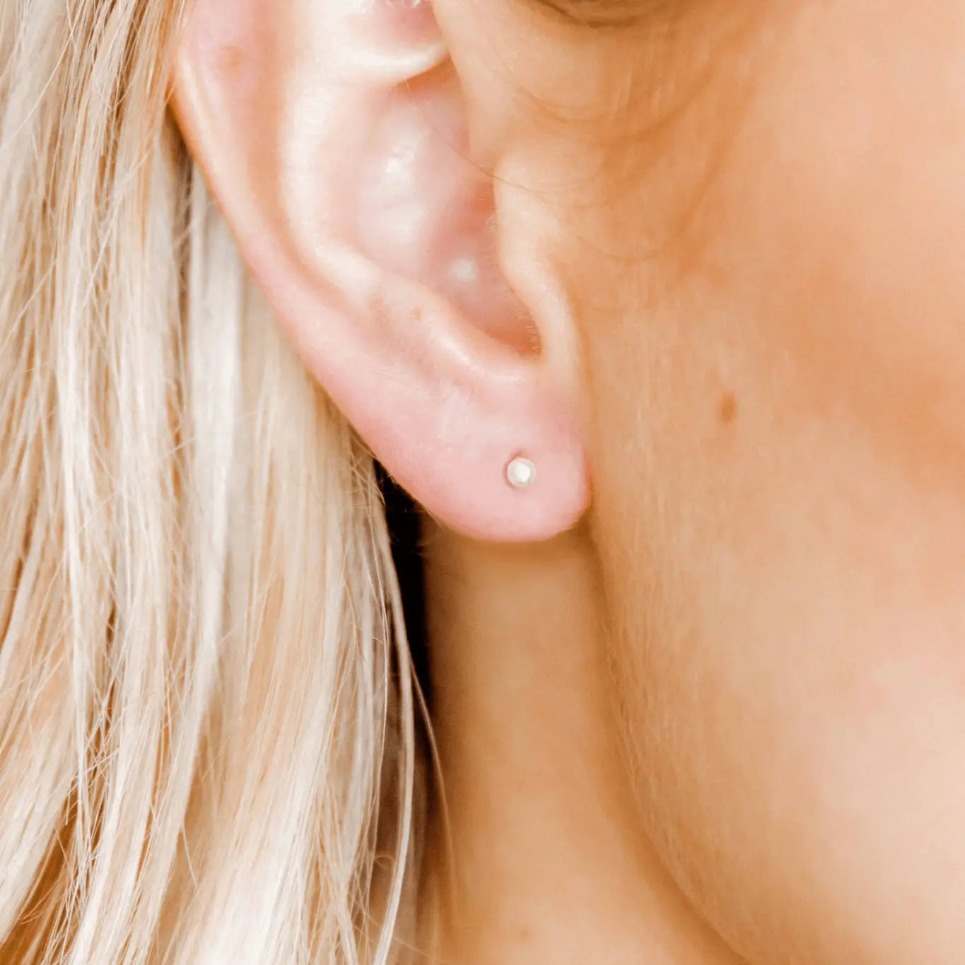 Close-up of an ear wearing a small pearl earring with blonde hair.