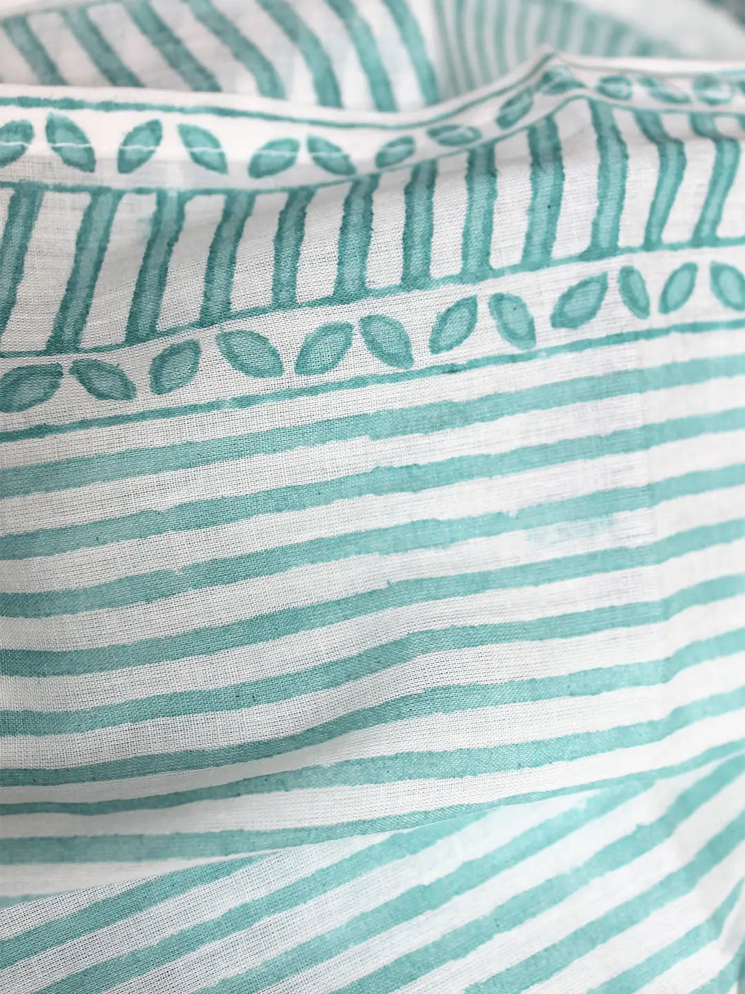 Close-up of fabric with teal stripes and leaf patterns on a white background
