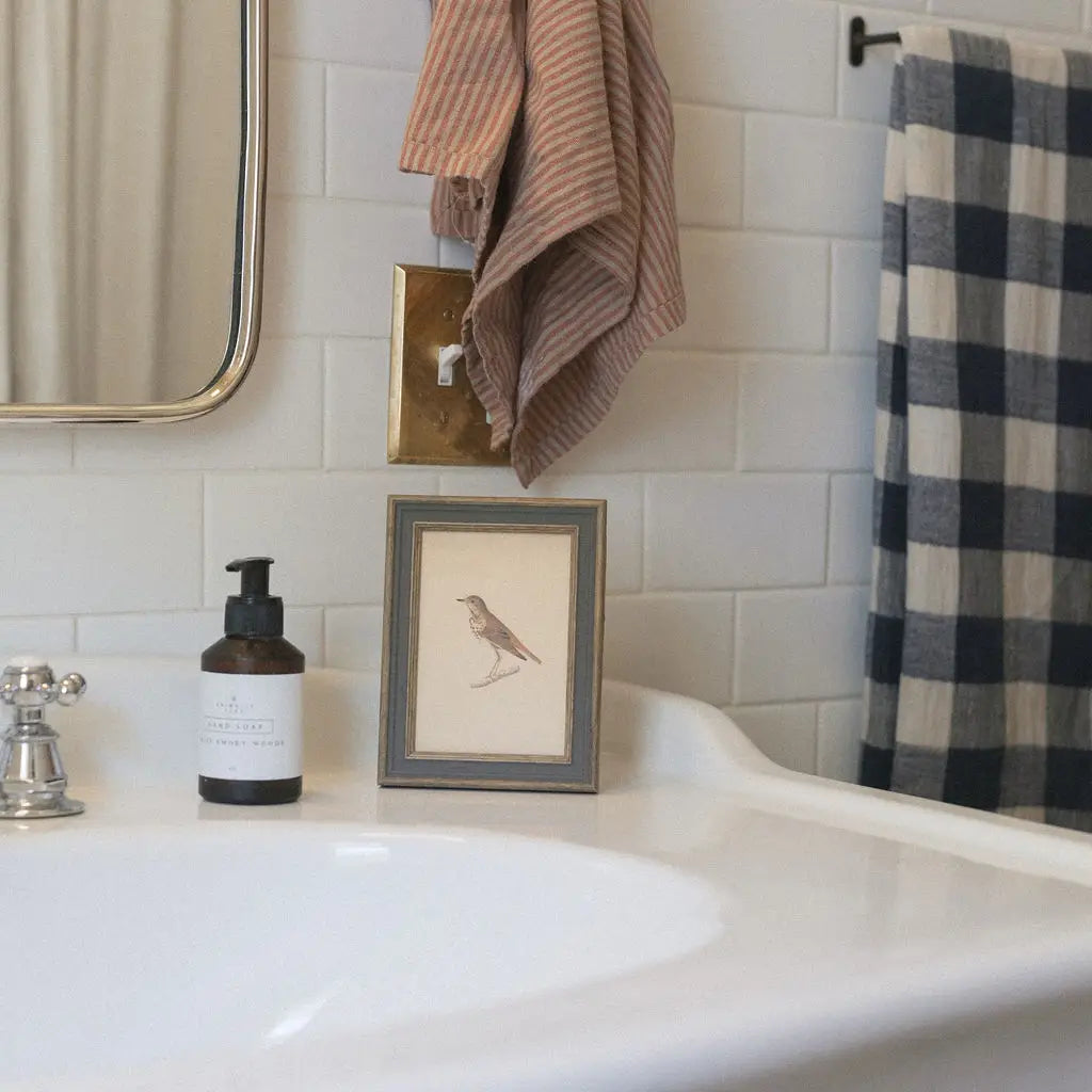 Bathroom counter with soap dispenser, framed picture, and towels on a tiled wall.