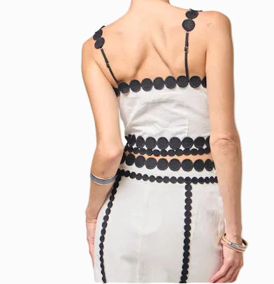 Woman wearing a white dress with black embellishments on a plain background