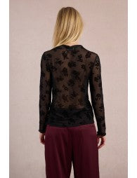 Person wearing a black patterned top and burgundy pants on a beige background