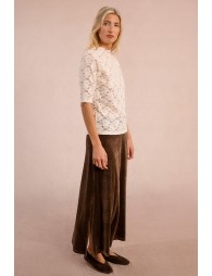 Woman wearing a white lace top and brown wide-leg pants on a plain background