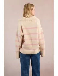 Person wearing a beige and pink striped sweater with blue jeans on a plain background