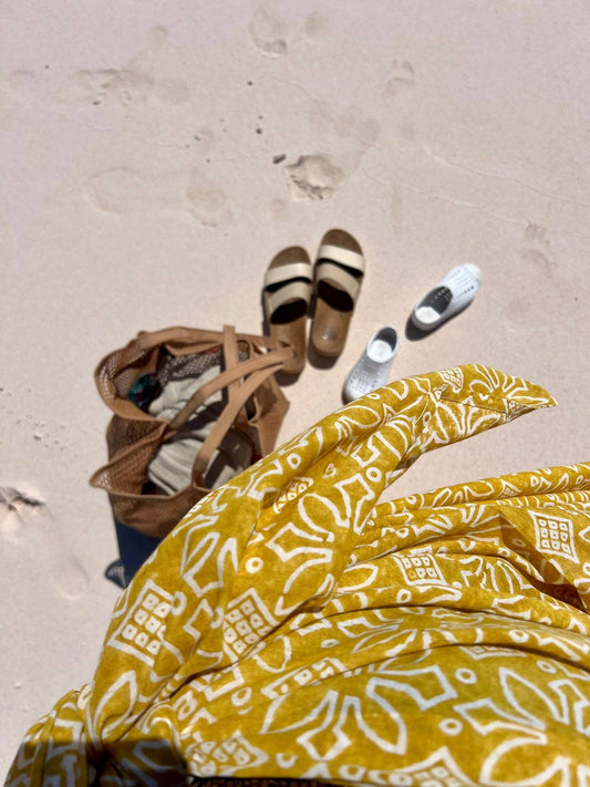Yellow patterned gloves on a sandy surface with sandals and flip-flops in the background.