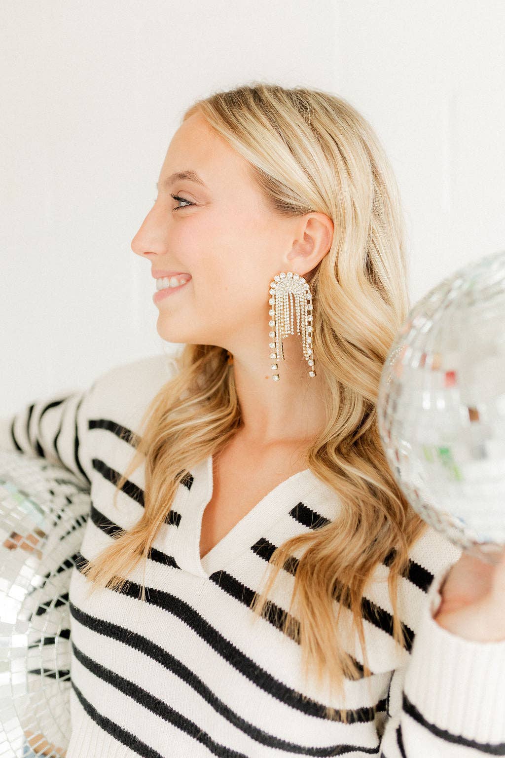 Woman wearing a black and white striped sweater and large tassel earrings, holding a disco ball.