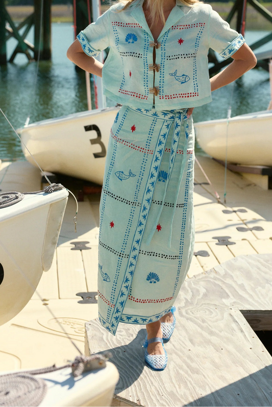 Woman in a light blue dress with whale pattern standing on a dock with boats in the background