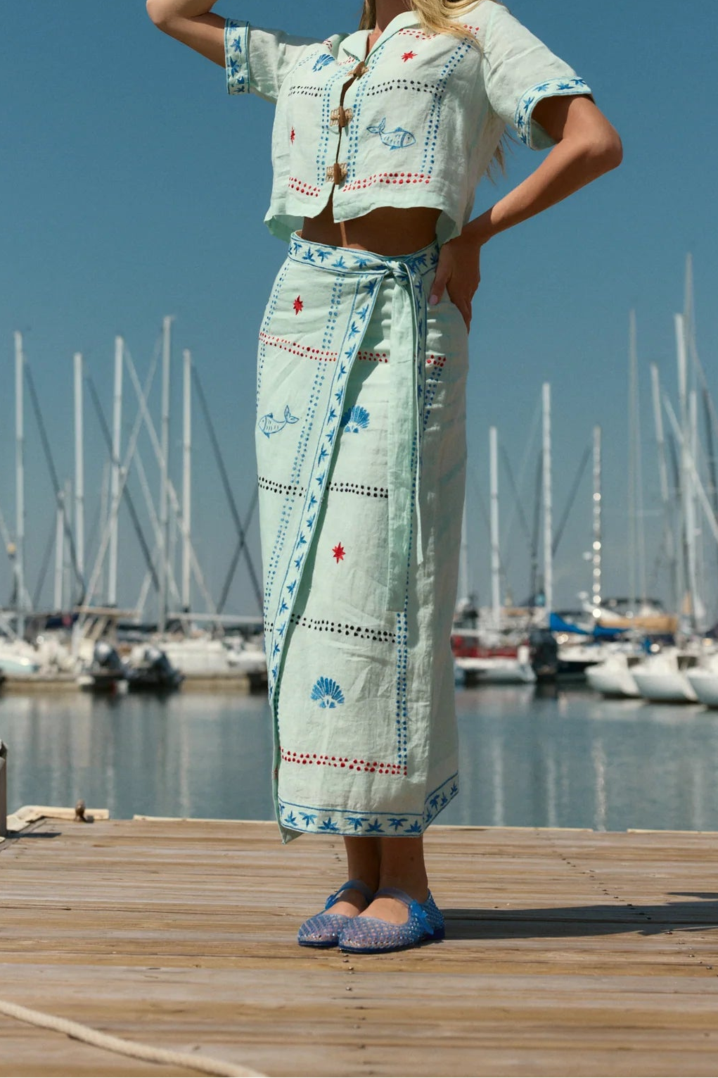 Woman in a light blue outfit standing on a dock with sailboats in the background