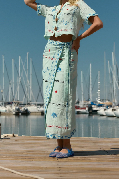 Woman in a light blue outfit standing on a dock with sailboats in the background