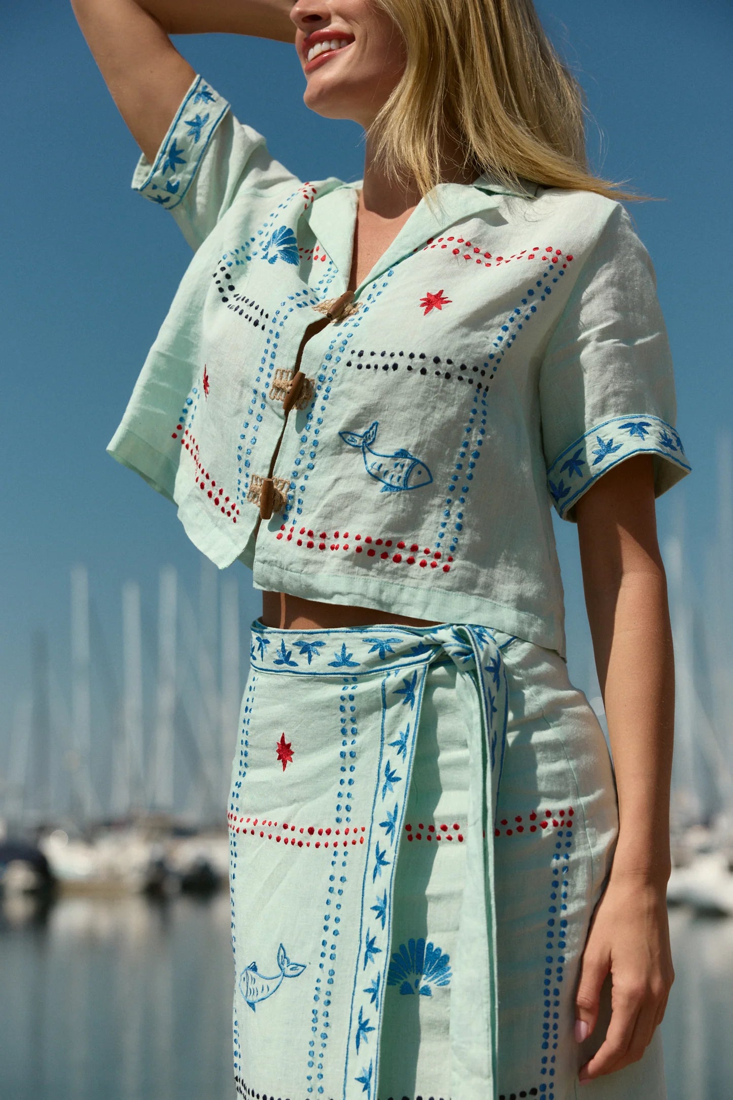 Woman wearing a light blue embroidered outfit with a marina in the background