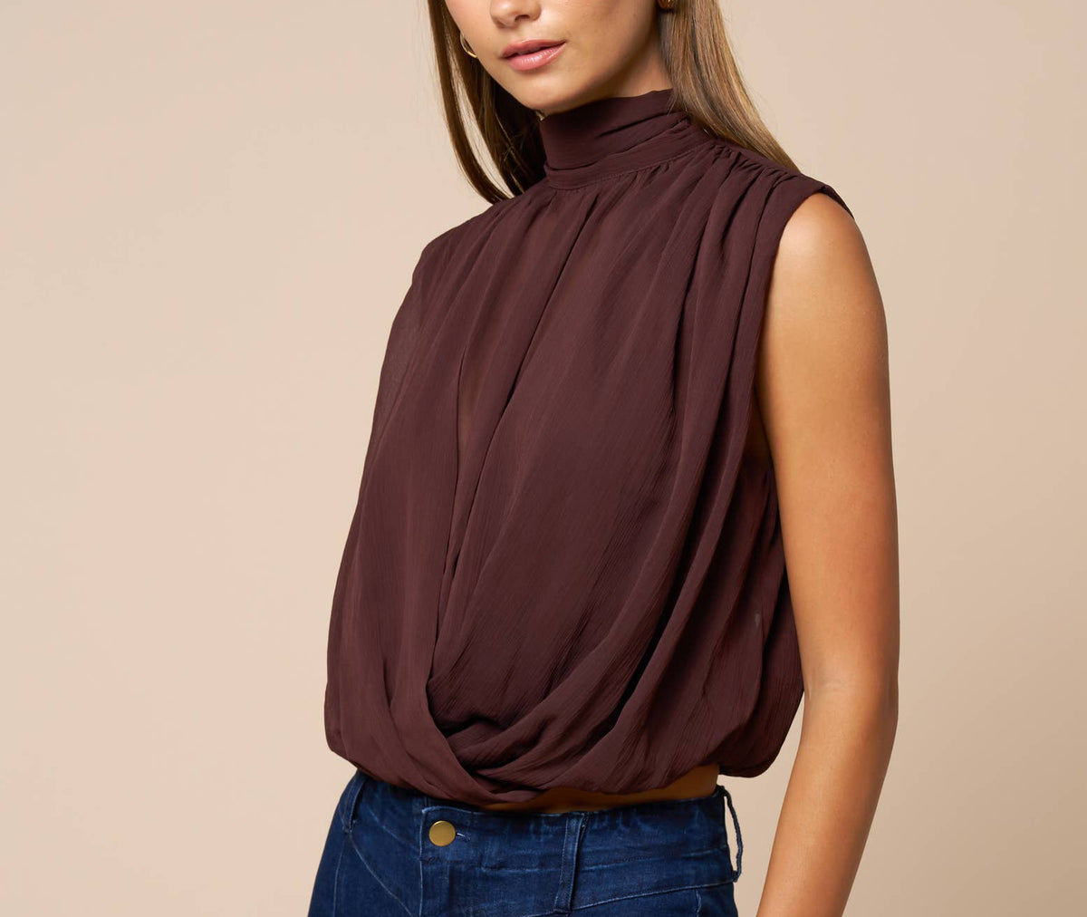 Woman wearing a brown sleeveless top and blue pants against a beige background