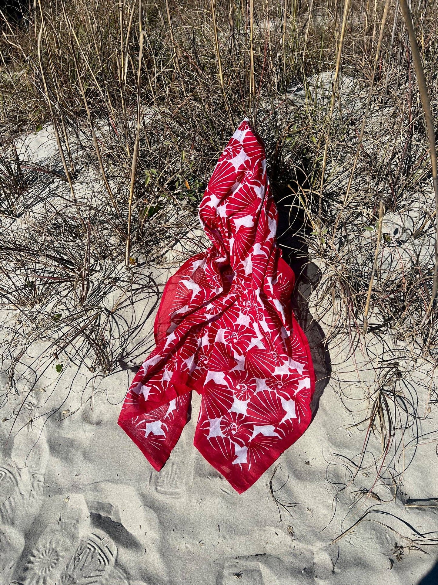 Red fabric with white patterns on a sandy ground with dry grass