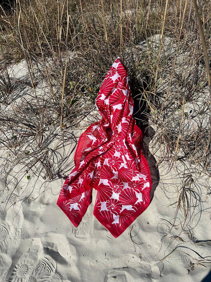 Red fabric with white patterns on a sandy ground with dry grass
