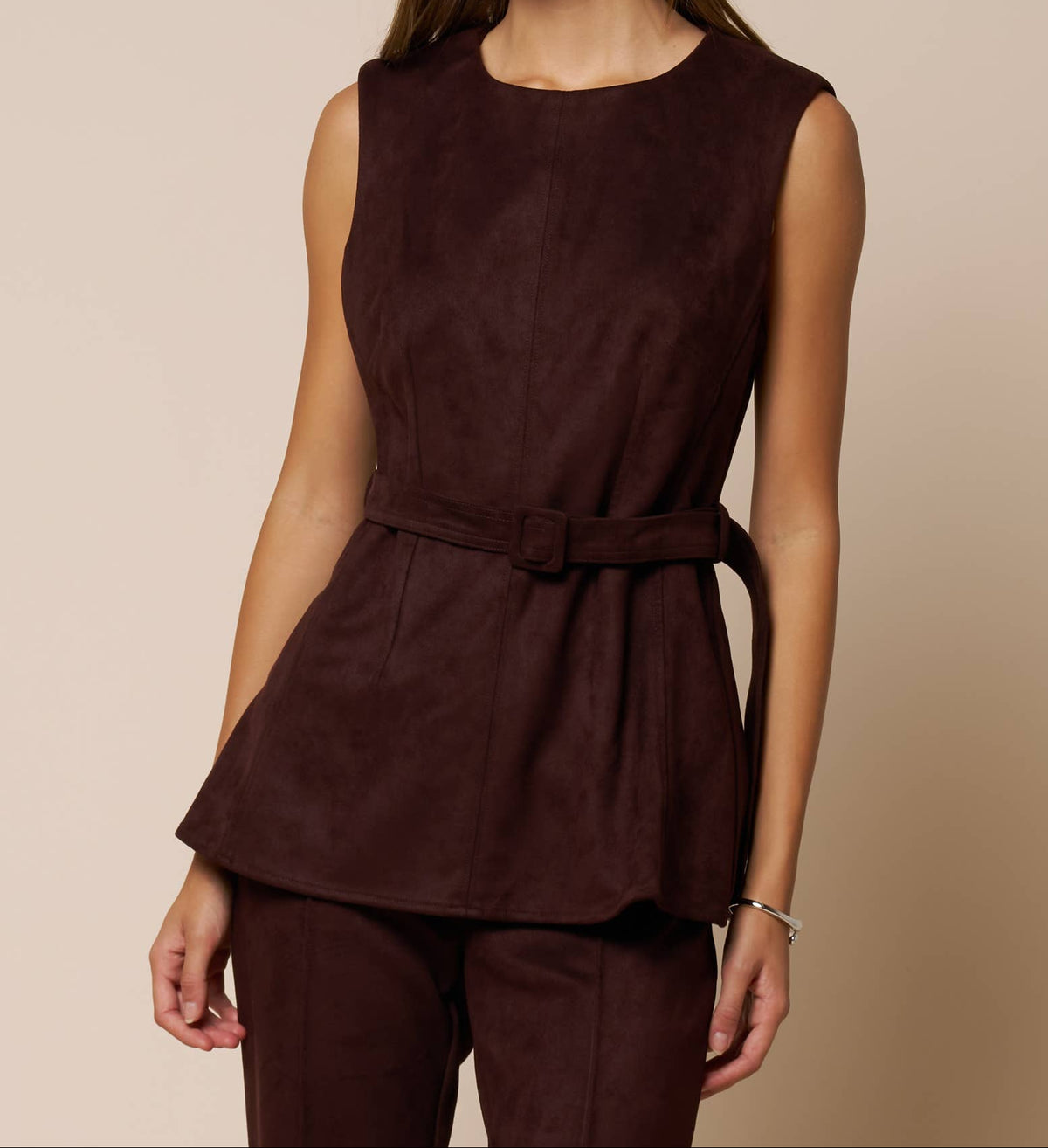 A woman modeling a sleeveless dark brown peplum top with a matching waist tie belt, paired with matching dark brown trousers, against a solid beige background.