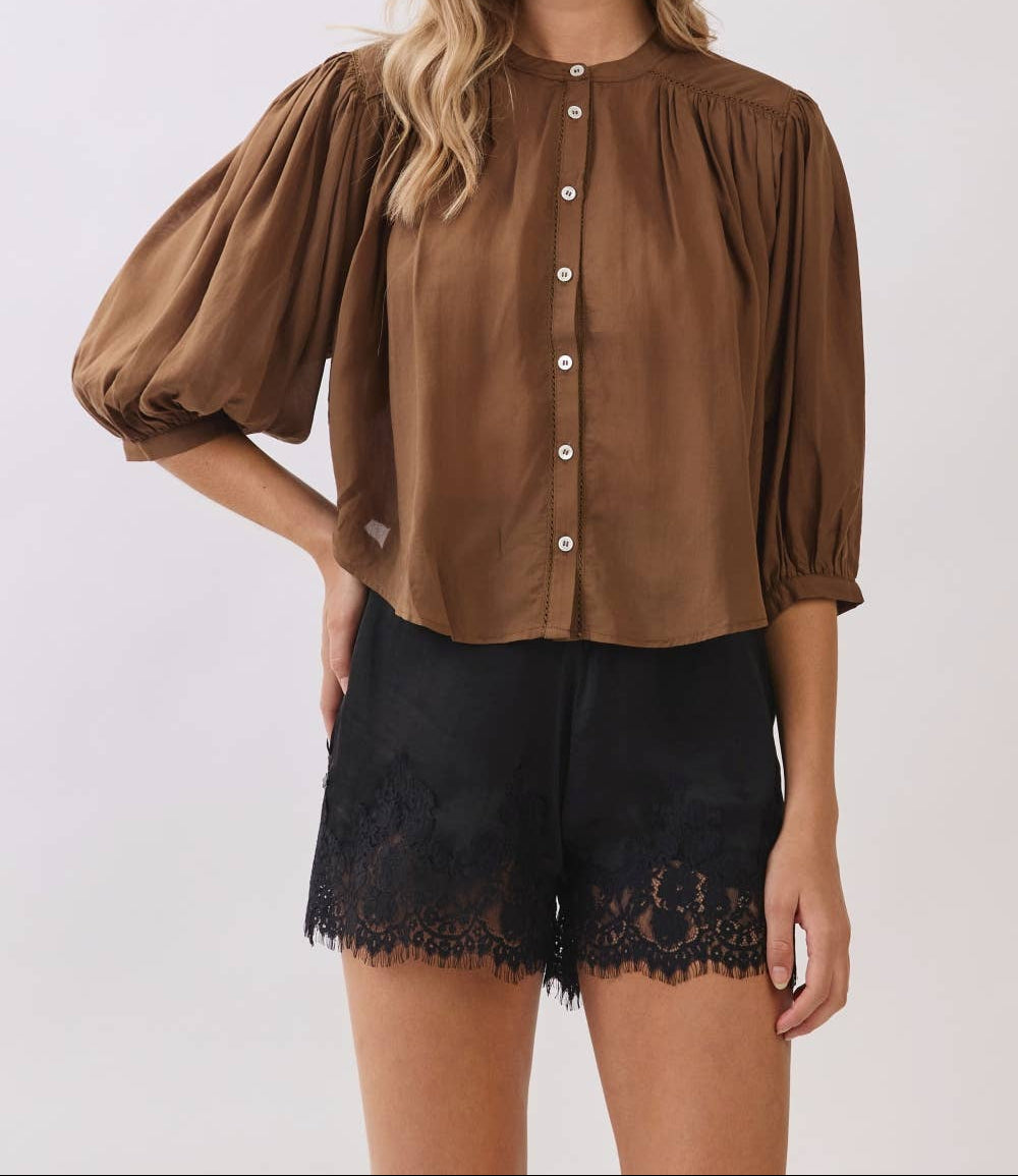 Woman wearing a brown blouse with puffed sleeves and black lace shorts on a white background